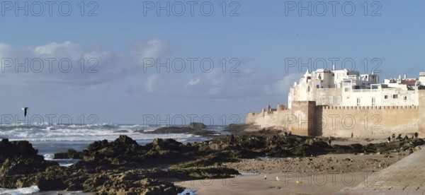 View of coastal landscape with city walls of Essaouira, waves and a small sandy beach with big