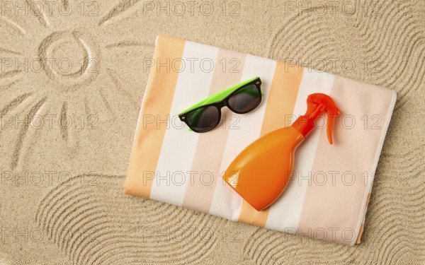 Drawing on the sand, sun and waves, sunglasses, with an orange bottle, beach towel, sun spray, on