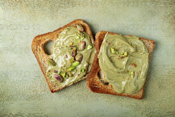 Two slices of toasted bread, topped with pistachio paste and sprinkled with pistachios, spread on a