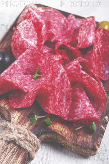 Sliced salami sausage, on a wooden chopping board, decorated with olives and herbs, close-up, no