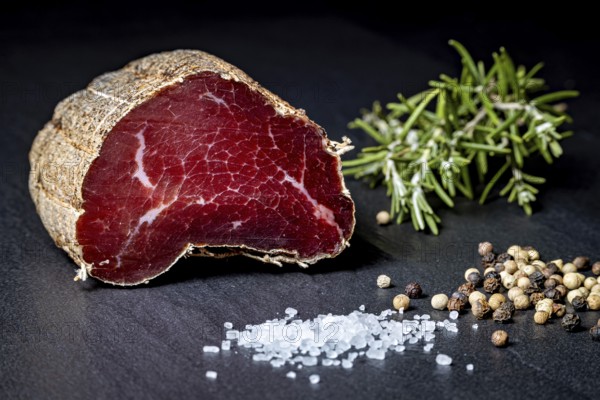 Delicate sausage piece on slate plate with salt and peppercorns, delicatess ham fresh from the