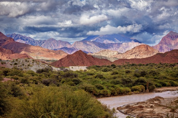 River flows through green vegetation against a mountain backdrop with red hills, the landscape and