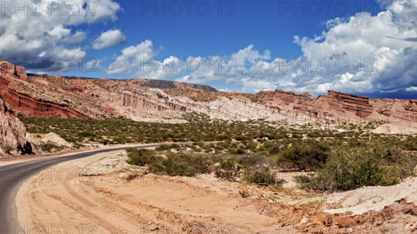 Road snakes through red rocky landscape under a cloudy sky, the landscape and colorful rock