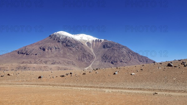 A bizarre mountain with a snow-capped summit rises above the dry desert, the landscape and colorful