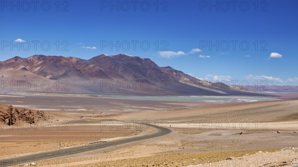 A long road snakes through an arid desert landscape with distant mountains, the countryside and