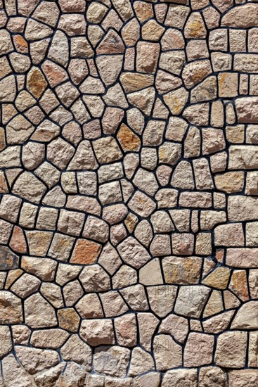 Irregular natural stone wall with brown-beige stones in rustic pattern, a natural stone wall as a
