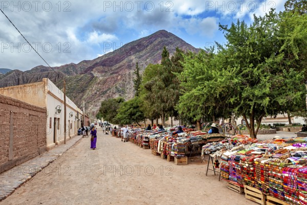A market with colorful fabrics along a street nestled in a mountainous landscape, tourist and