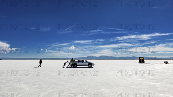 People push a car on a wide salt lake under a blue sky, The Salar de Cauchari salt pan near Salta