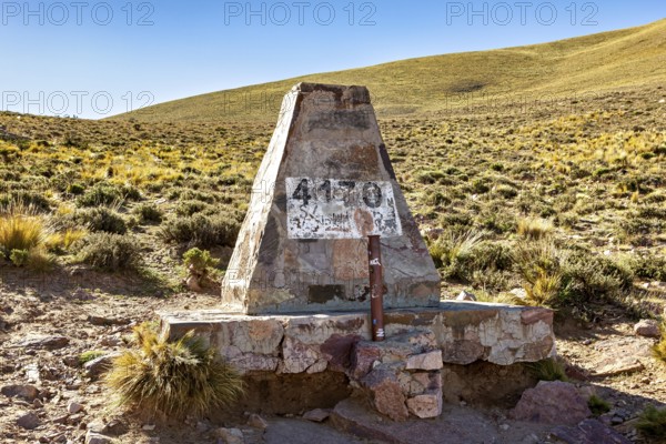 Stone pyramid with altitude marker at 4130 meters, surrounded by dry desert landscape under blue