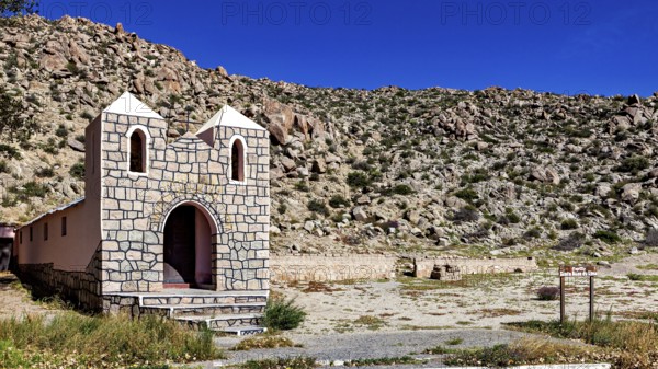 Small chapel in a wide desert landscape with rocky surroundings under bright blue sky, The chapel