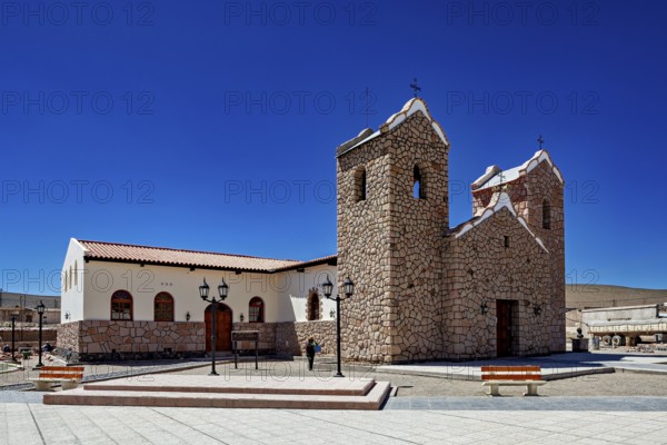 Stone church with two towers under clear blue sky in an open square with lanterns, Parroquia San