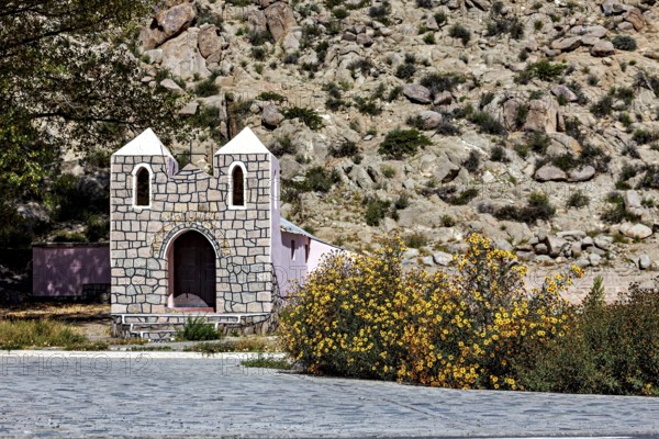 Small stone house in a desert area with yellow flowers in the foreground against a rocky mountain