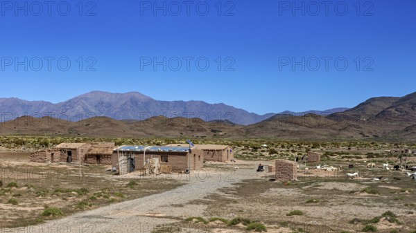 Cabins in an open desert landscape with dry soil and mountains in the background, San Antonio de