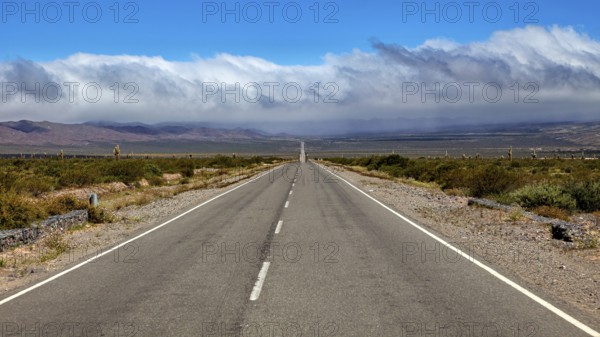 Endless road leads to distant mountains under dramatic clouds, The landscape of the Quebrada with