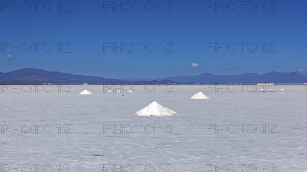 Wide salt desert with salt formations in the foreground and mountains on the horizon under clear