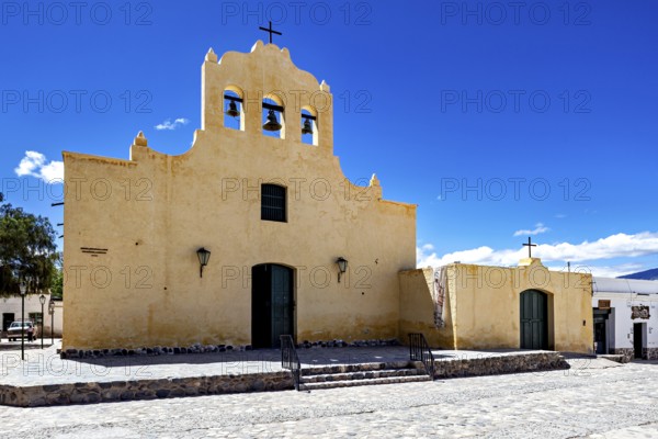 Yellow church with bell tower and cross against a clear sky, colonial style of architecture,