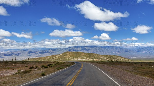 An empty, winding road leads through a vast desert landscape under a cloudy sky, The landscape of