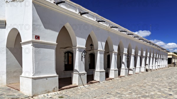 White building with colonial-style arcades under clear blue sky, The arcades of Cachi in Argentina