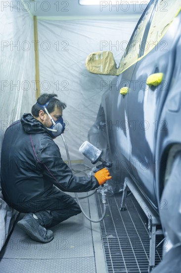 Auto body technician wearing mask and gloves sprays primer onto a car door panel inside a