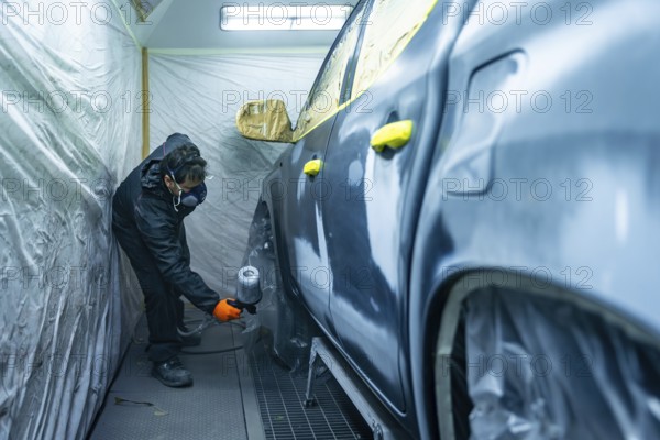 Auto body technician working in a repair shop, carefully applying paint primer to a vehicle door