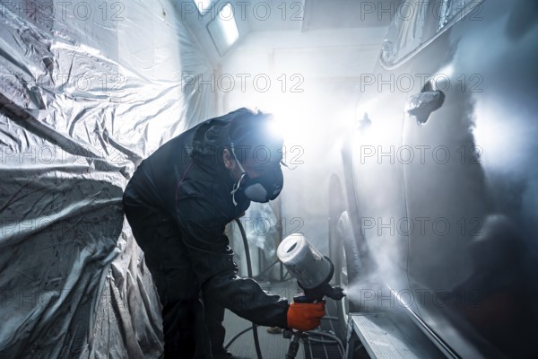 Auto body painter wearing a respirator mask and protective suit, carefully applying a fresh coat of