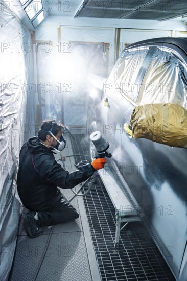 Professional auto body mechanic kneeling while applying primer or paint to a passenger cars side