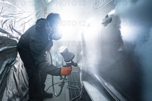 Auto mechanic applying primer paint to a car body panel using a spray gun in a well lit automotive