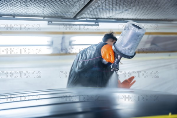 Auto body technician wearing protective gloves painting a vehicle car roof using a spray gun in a