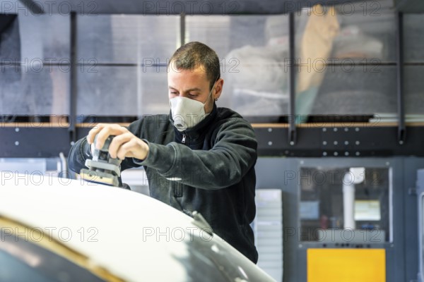 Auto body technician wearing a respirator mask using an orbital sander to prepare a car surface for