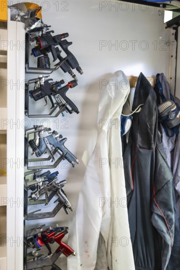 Modern spray guns and protective gear, including a disposable suit and a respirator mask, hanging