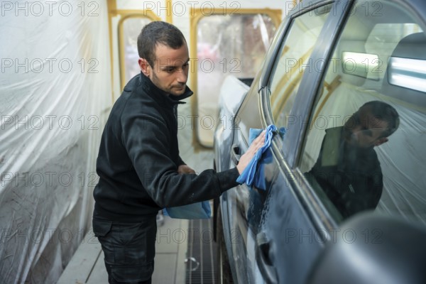 Man carefully wiping car body panels with a blue microfiber cloth inside a professional spray