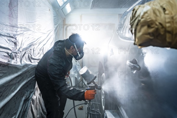 Professional automotive technician applying a fresh coat of paint to a vehicle in a specialized
