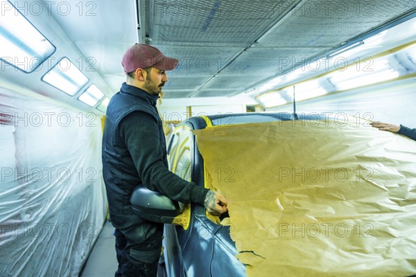 Skilled technician carefully masking vehicle with brown paper and tape, preparing it for a