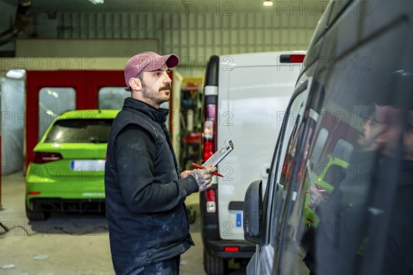 Mechanic holding a clipboard and pen while inspecting a commercial van in a car body and paint