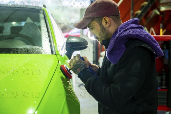 Mechanic meticulously polishing a vibrant green car body with a rotary polisher, improving its