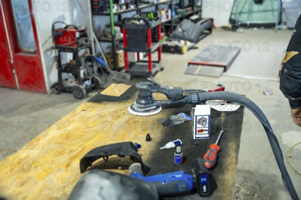 Orbital sander, hand tools, and car parts sitting on a wooden workbench inside a busy automotive