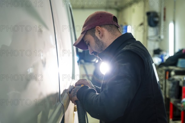 Auto body technician focused on sanding a vehicle's surface with an orbital sander, preparing the