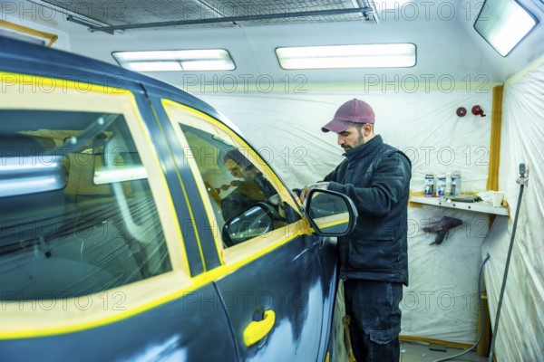 Auto repair technician carefully applying masking tape to a car door and window, protecting parts