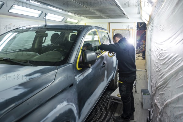 Automotive technician preparing a vehicle for painting by carefully applying protective masking