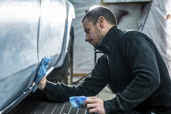 Focused mechanic carefully smooths and cleans car body surface before painting inside a modern auto