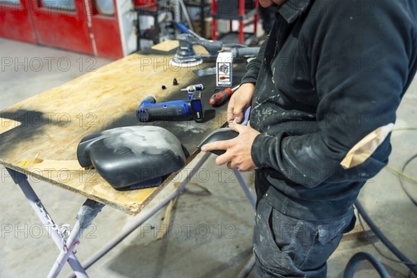 Auto body repairman meticulously sanding a car part, preparing surfaces for paint spraying,