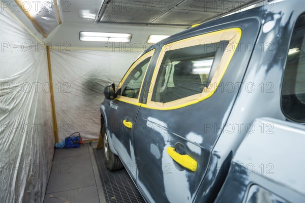 Vehicle in a body shop prepped for painting, masked with tape over windows and trim, primed and