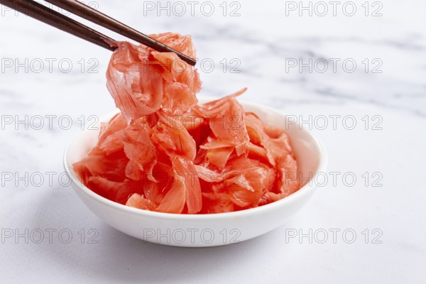 Pickled ginger, with chopsticks, in a small white bowl, on a marble countertop, close-up, no people