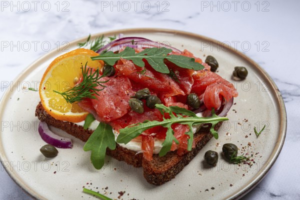 Sandwich with freshly smoked salmon, on black bread, with cottage cheese, with herbs and red
