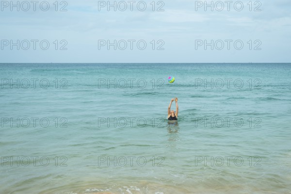 A young woman engaged in playful activity with a colorful ball in the calm ocean water in Thailand,