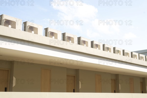 A row of air conditioning units on a modern building rooftop against a clear blue sky in Thailand.