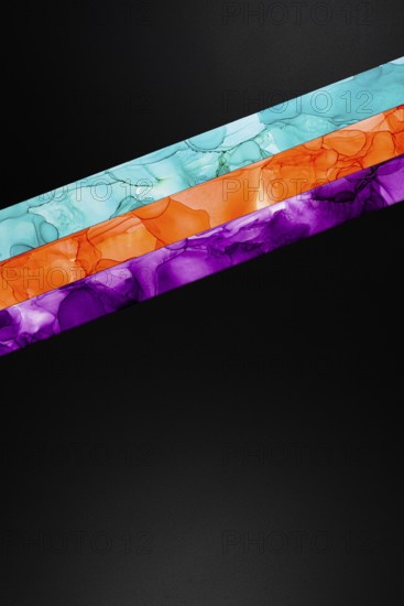 Vibrant diagonal colors inks stripes of teal, orange, and purple on a dark background. This