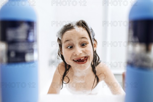 A joyful child enjoys bath time, playfully covered in foam and surrounded by bubbles, exuding