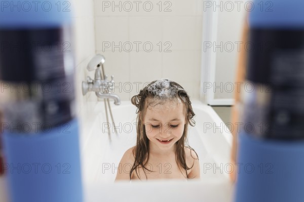 A joyful child enjoys a bath, crowned with soap bubbles. Surrounded by shampoo bottles, the playful