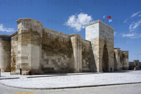 Impressive stone wall with high gate under blue sky with waving flags, Sultanhani caravanserai, on
